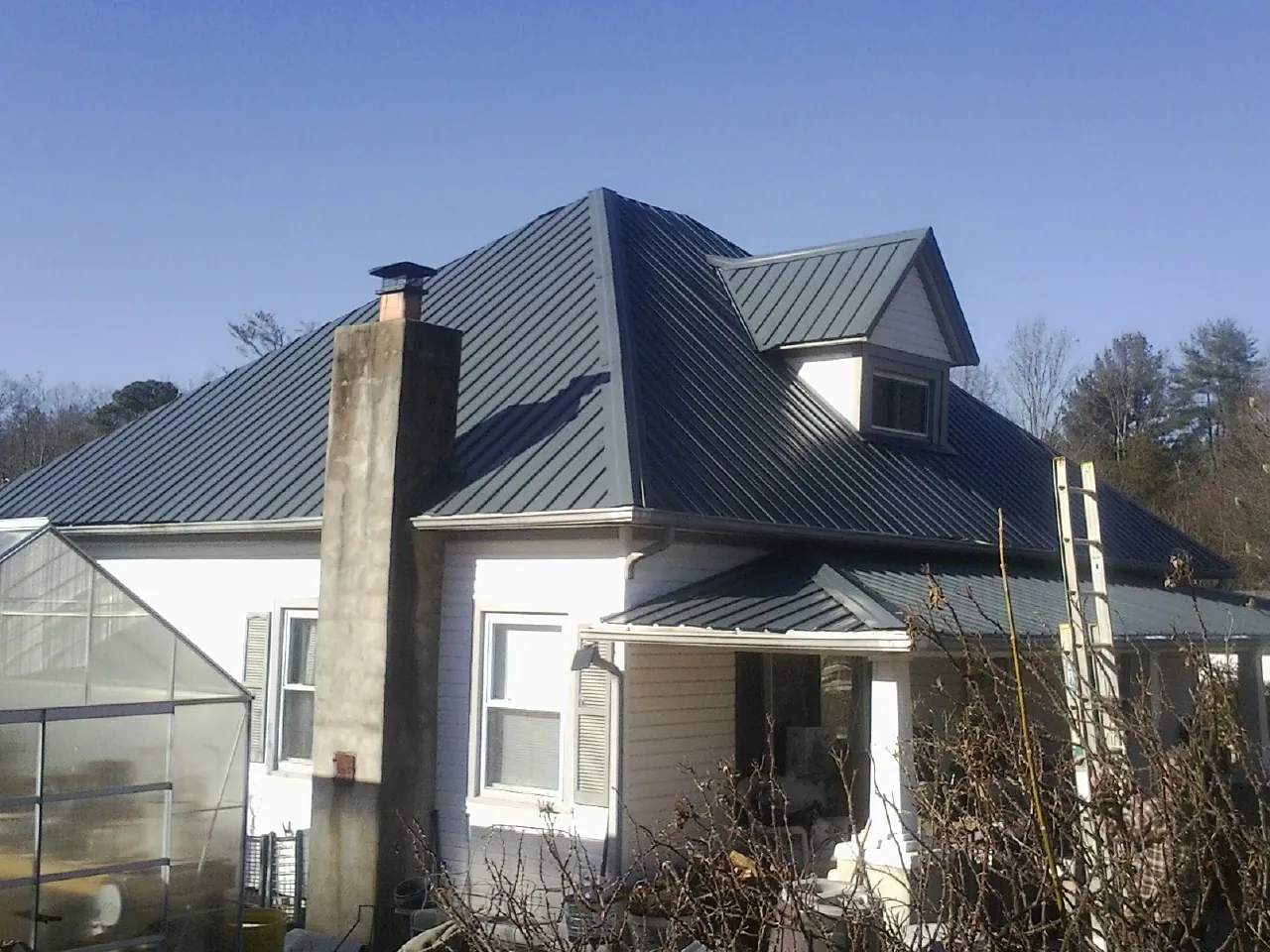 Dark blue standing seam metal roof on a white farmhouse with dormer — Slate & Tile Roof Repair by Roofing Brothers in Plains