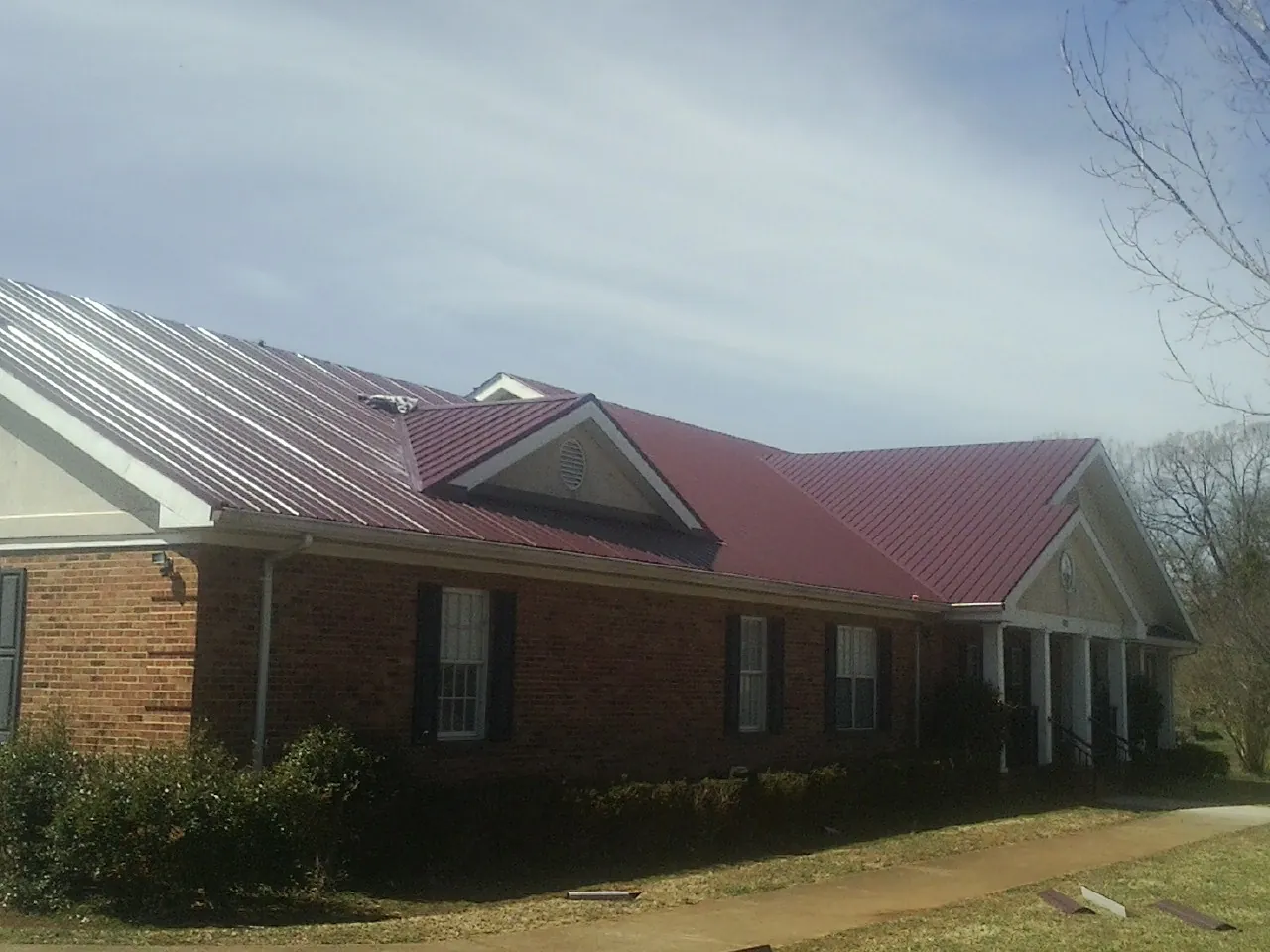 Red metal roof with gabled entries on a long brick building, from a Hail Damage Roof Repair job in Plains