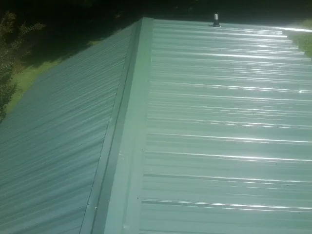 New green metal panels meeting at the ridge of a roof — Flat Roof Repair work by our crew in Plains